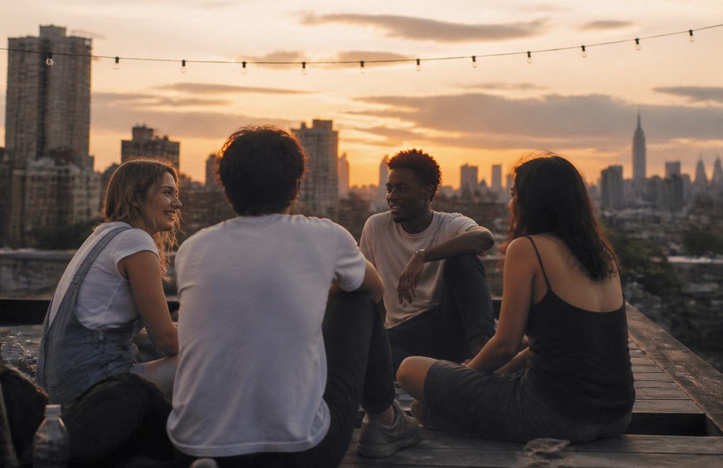 Four friends talking together on a rooftop as the sun sets behind the city